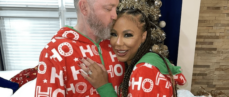 Couple in matching Christmas pajamas hugging indoors.